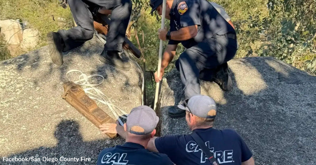 Firefighters working together on a rocky surface while handling a rope and equipment during a rescue operation.
