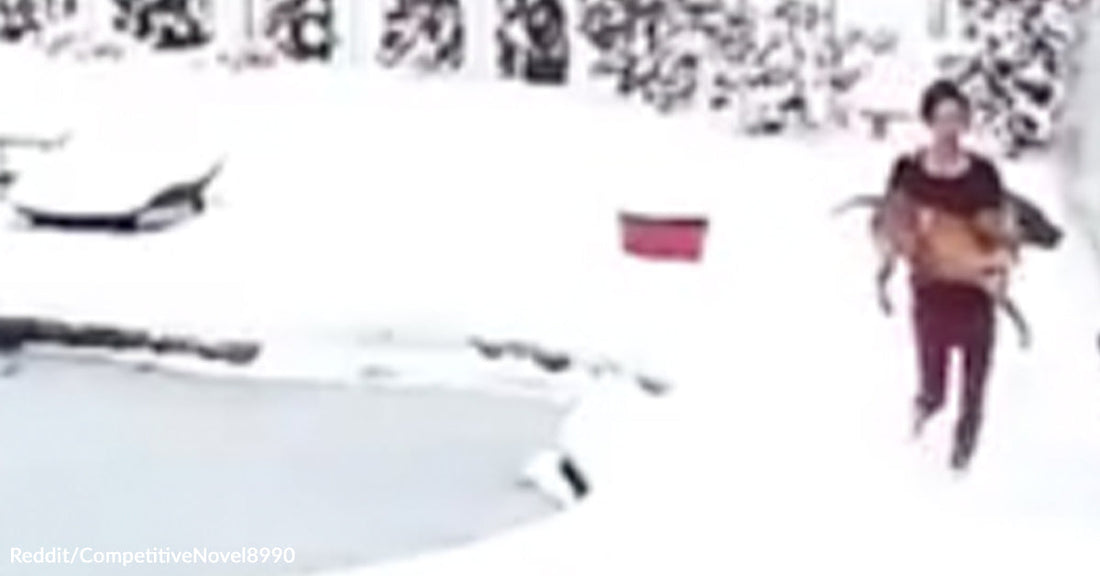 A person runs across snowy ground while carrying a dog away from a frozen pond.