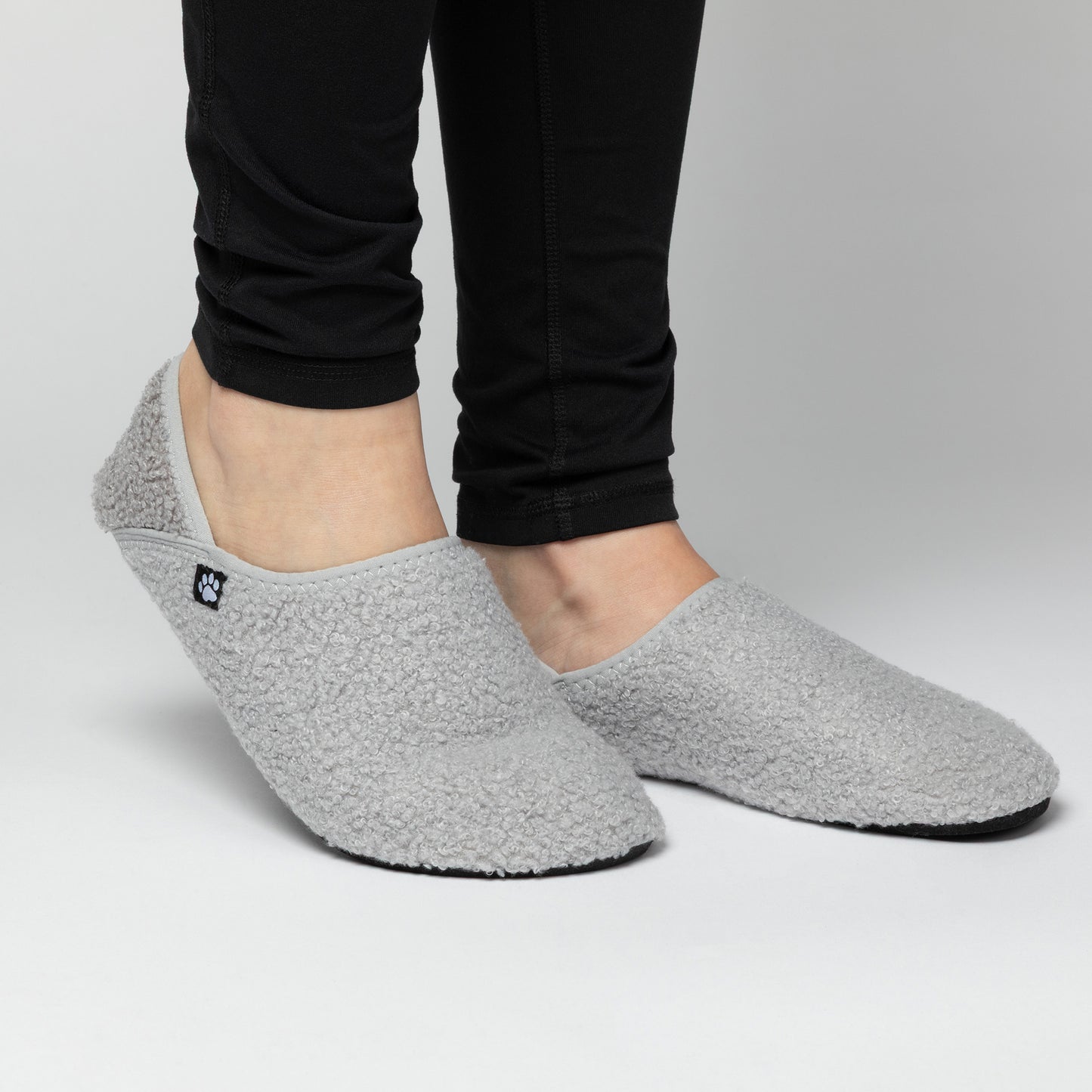 Gray slip-on shoes worn with black pants on a light gray background