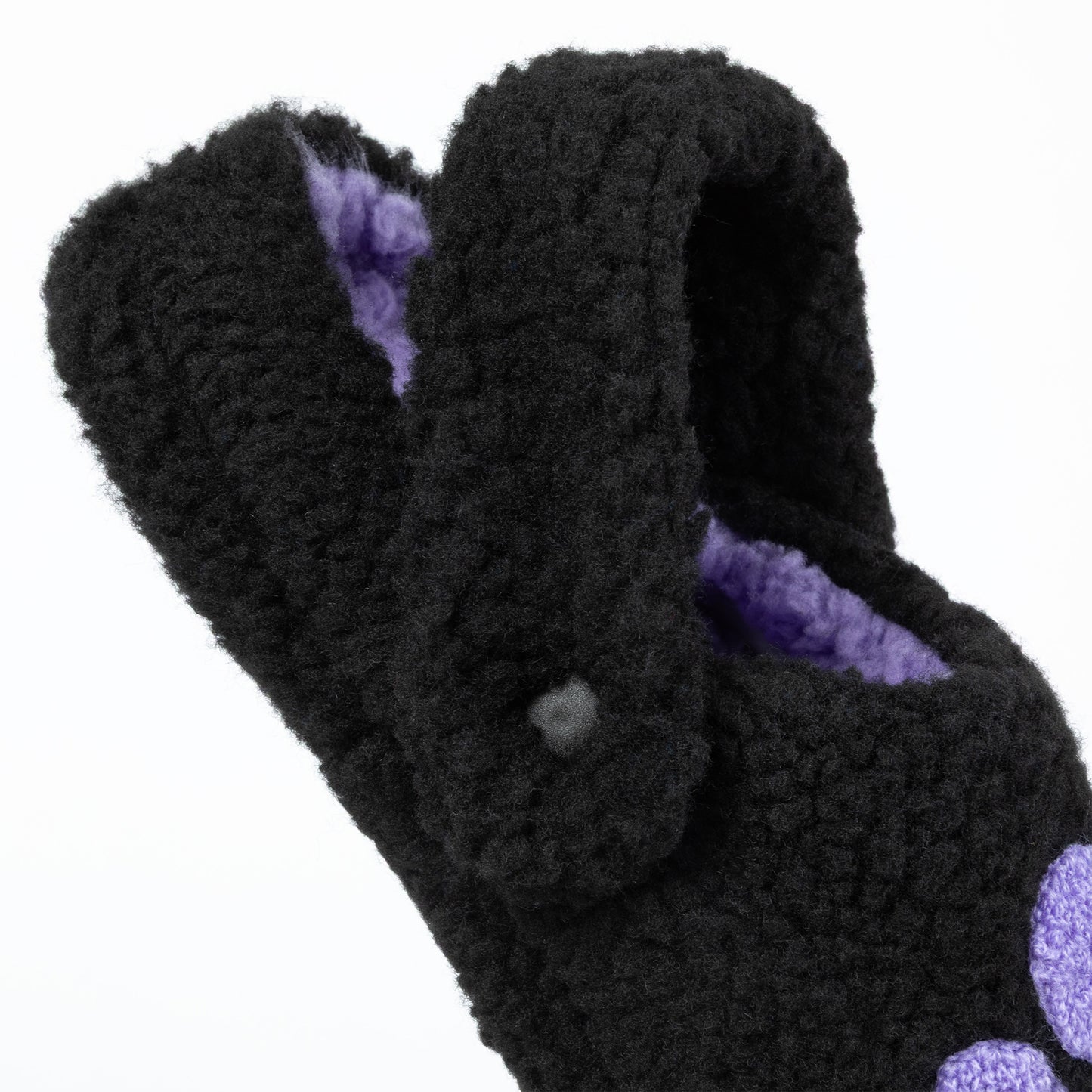 Black fuzzy slippers with purple interior on a white background
