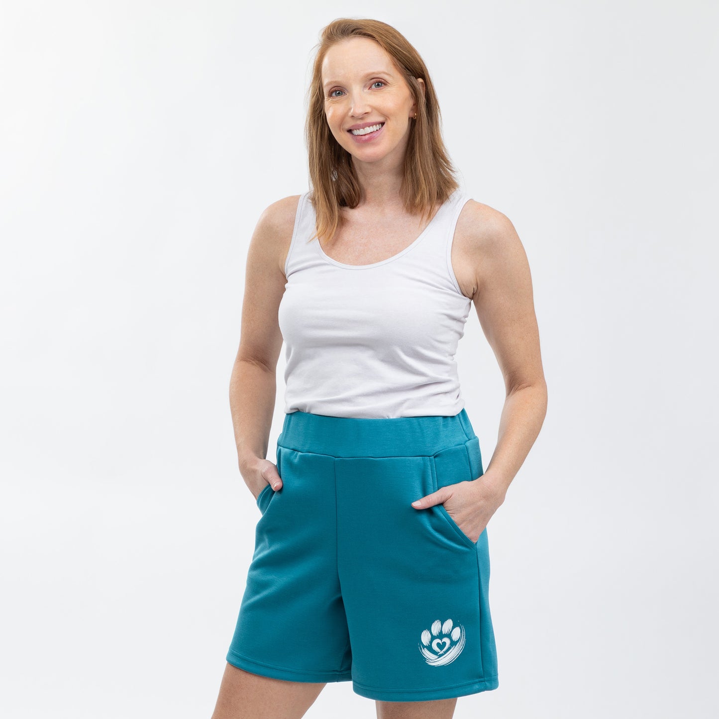Woman wearing teal shorts with a logo and a white tank top on a light gray background