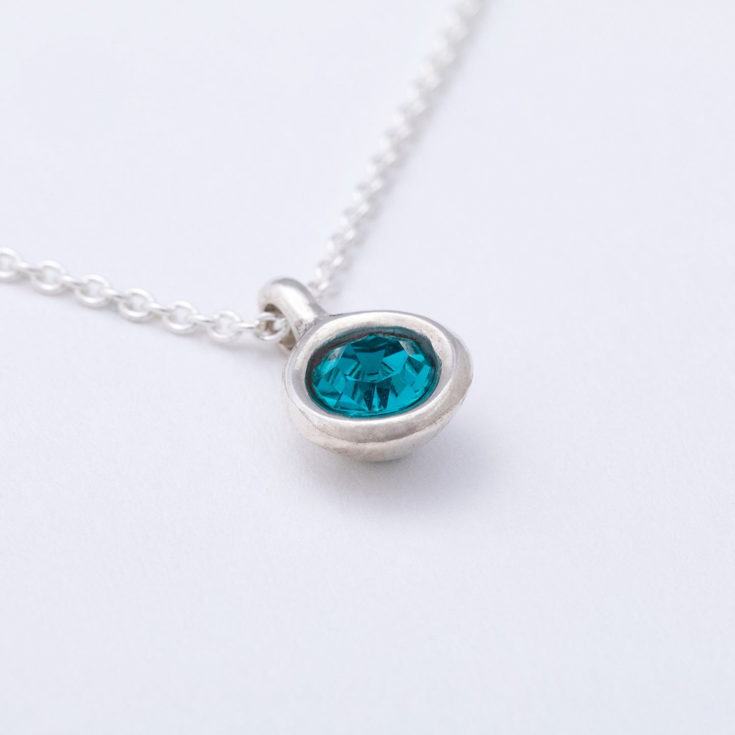 Silver necklace with a blue gemstone pendant on a white background
