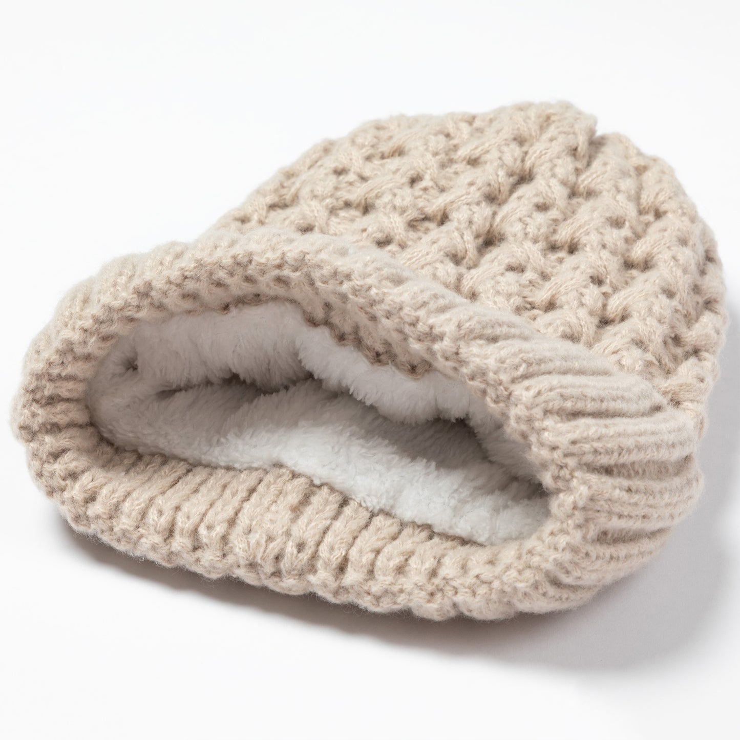 A chunky knit beanie hat in a warm beige color, featuring a thick white faux-fur lining visible inside the folded opening, set against a plain white background.