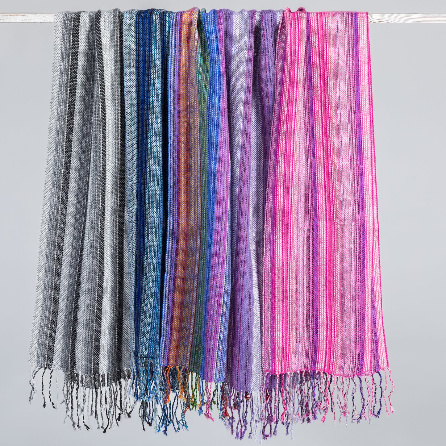 Handwoven alpaca scarves with multiple color stripes, hanging on a bar with fringe at the bottom.