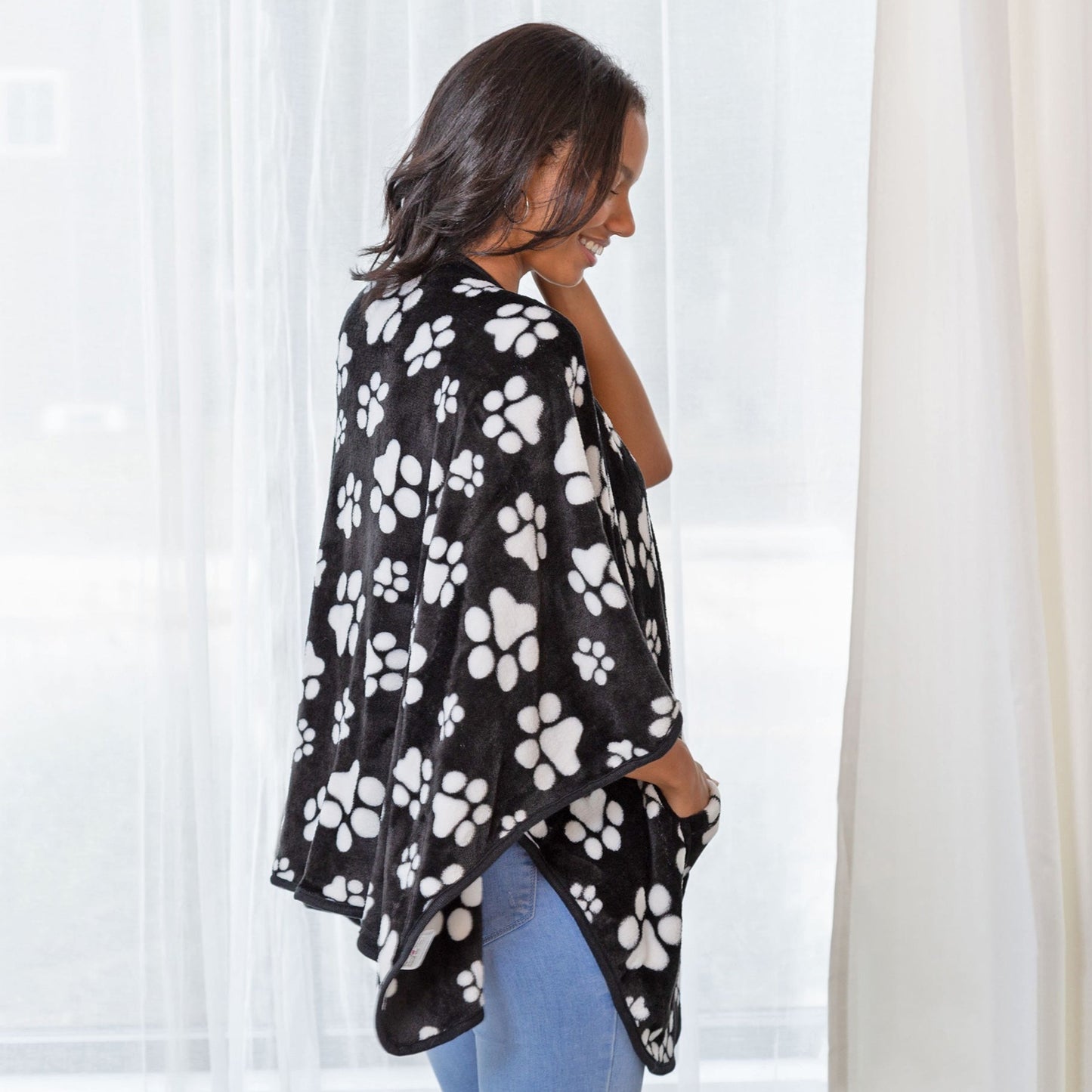A woman wearing a black and white paw print pocket shawl standing in front of white curtains.