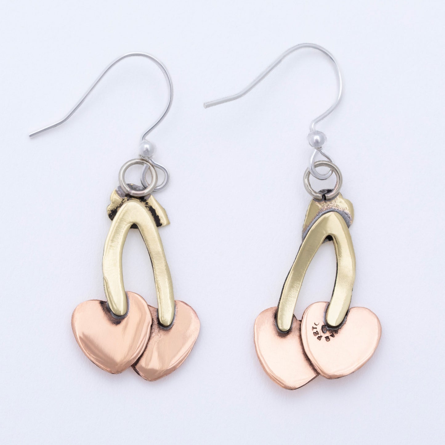 Pair of earrings with brass and copper heart-shaped/ cherry shaped pendants on a light background.