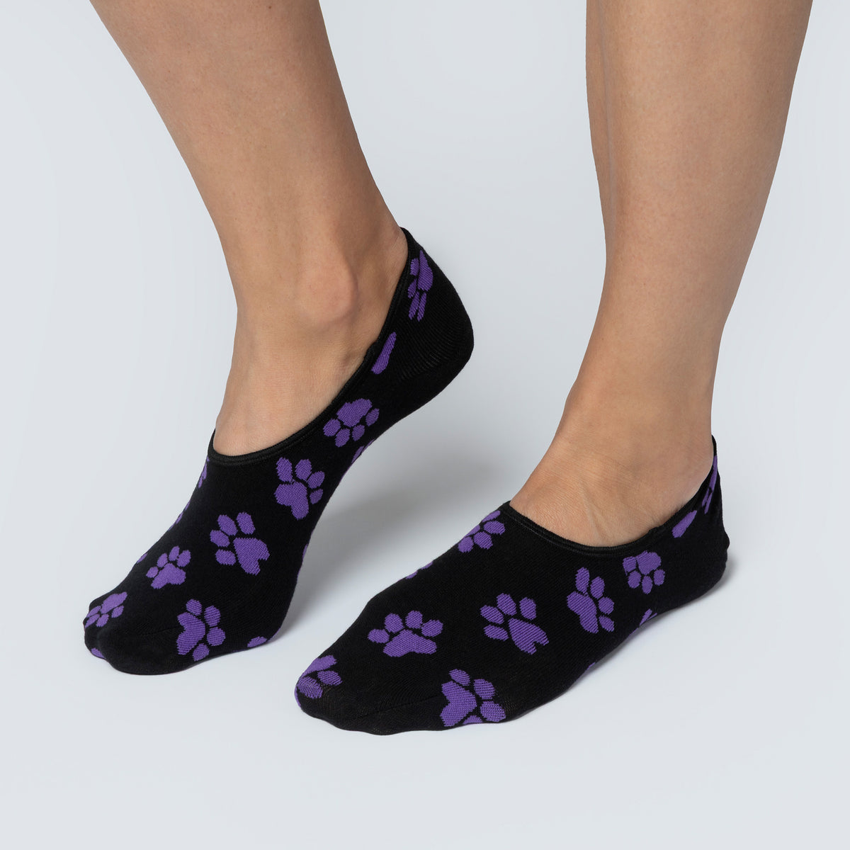 Black socks with purple paw prints worn by a person on a light gray background