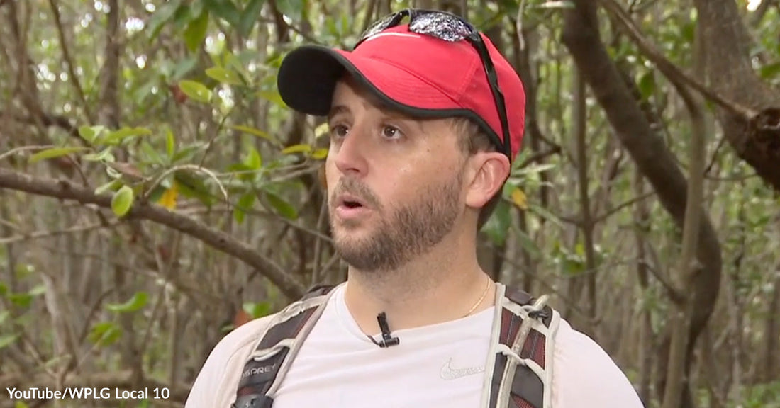 Man wearing a red cap and backpack speaking on camera in a mangrove forest.