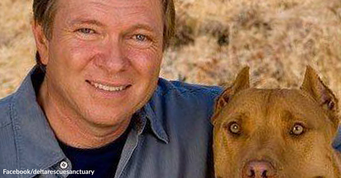 A man wearing a blue collared shirt next to a brown dog.
