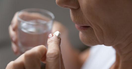 woman taking a white pill with glass of water in her hand