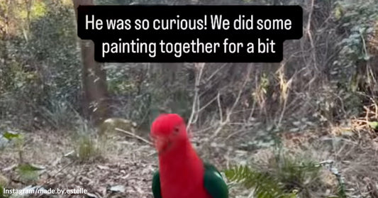 A red parrot amidst forest trees. Words on the image read, "He was so curious! We did some painting together for a bit."