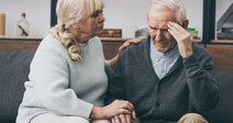 elderly couple with man holding his head