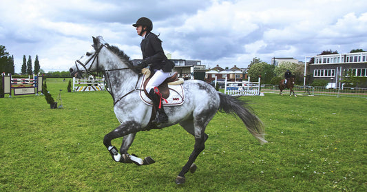 A rider on a gray horse gallops across a grassy field during an equestrian event.