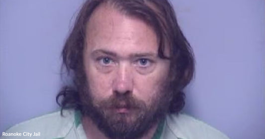 Mugshot of a bearded man against a plain light-purple background.