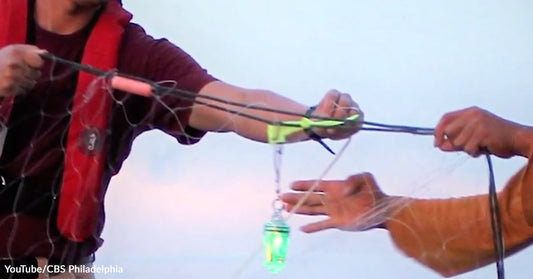 Two people on a boat adjusting a fishing net fitted with a glowing green light device during daylight.