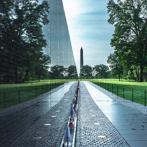 Long view along the Vietnam Veterans Memorial wall with the Washington Monument visible in the distance across the lawn.
