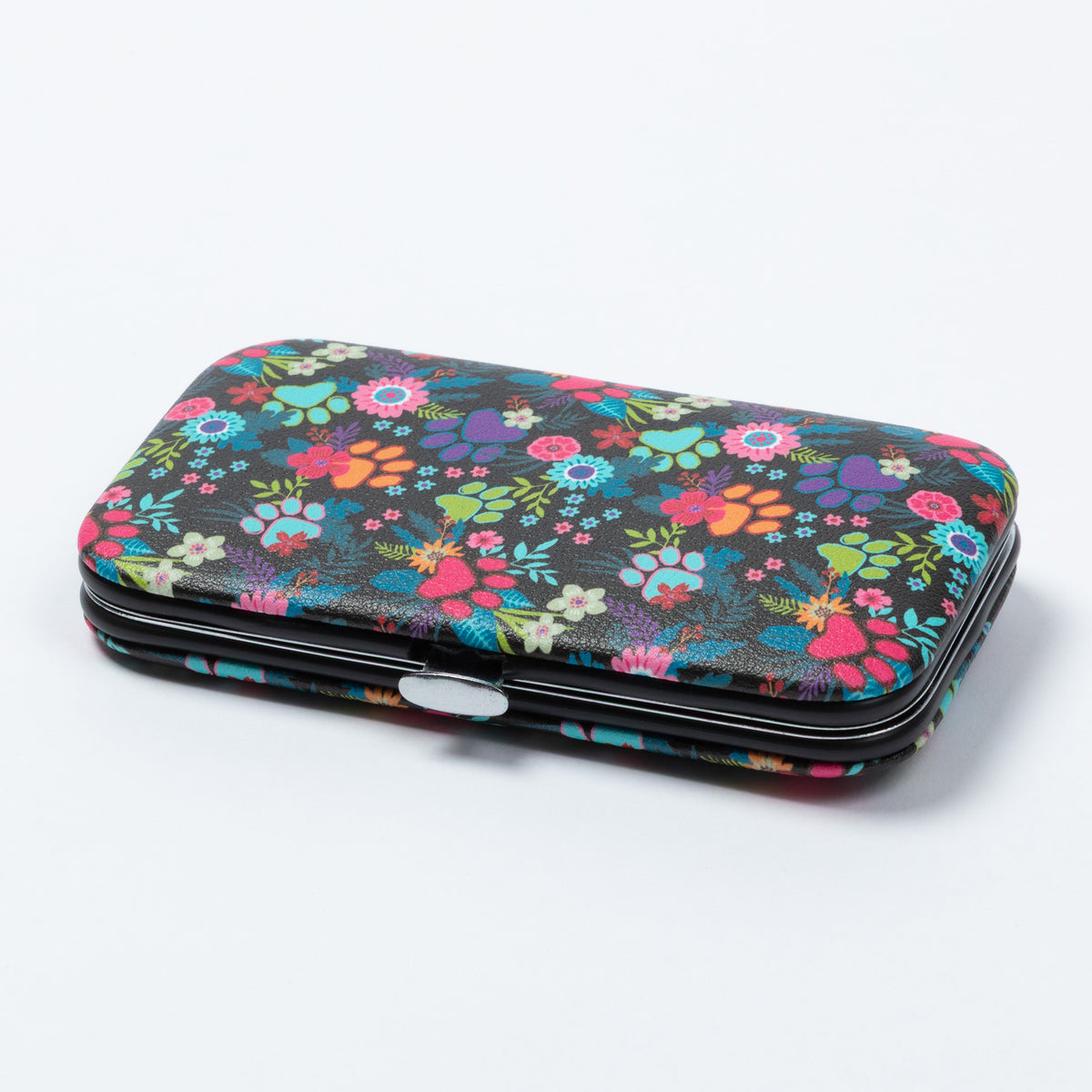 A rectangular manicure kit with a colorful floral and paw print pattern on a black background, featuring a silver metal clasp, photographed on a light gray studio background.