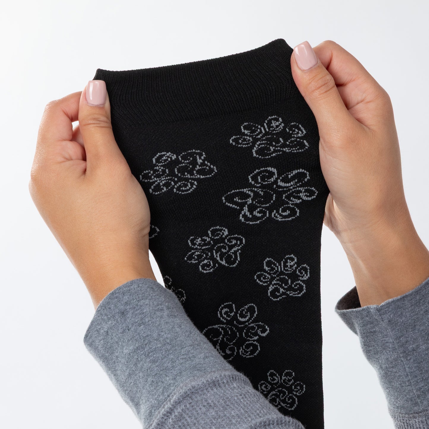 Hands holding up a stretchy black compression sock with white swirl paw prints against a white background.