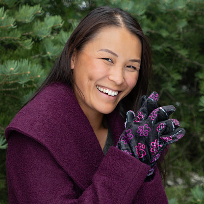 A woman, outside, wearing a coat and a pair of touchscreen technology fingertips warm black fleece gloves adorned with prink and violet elegant paw prints. 