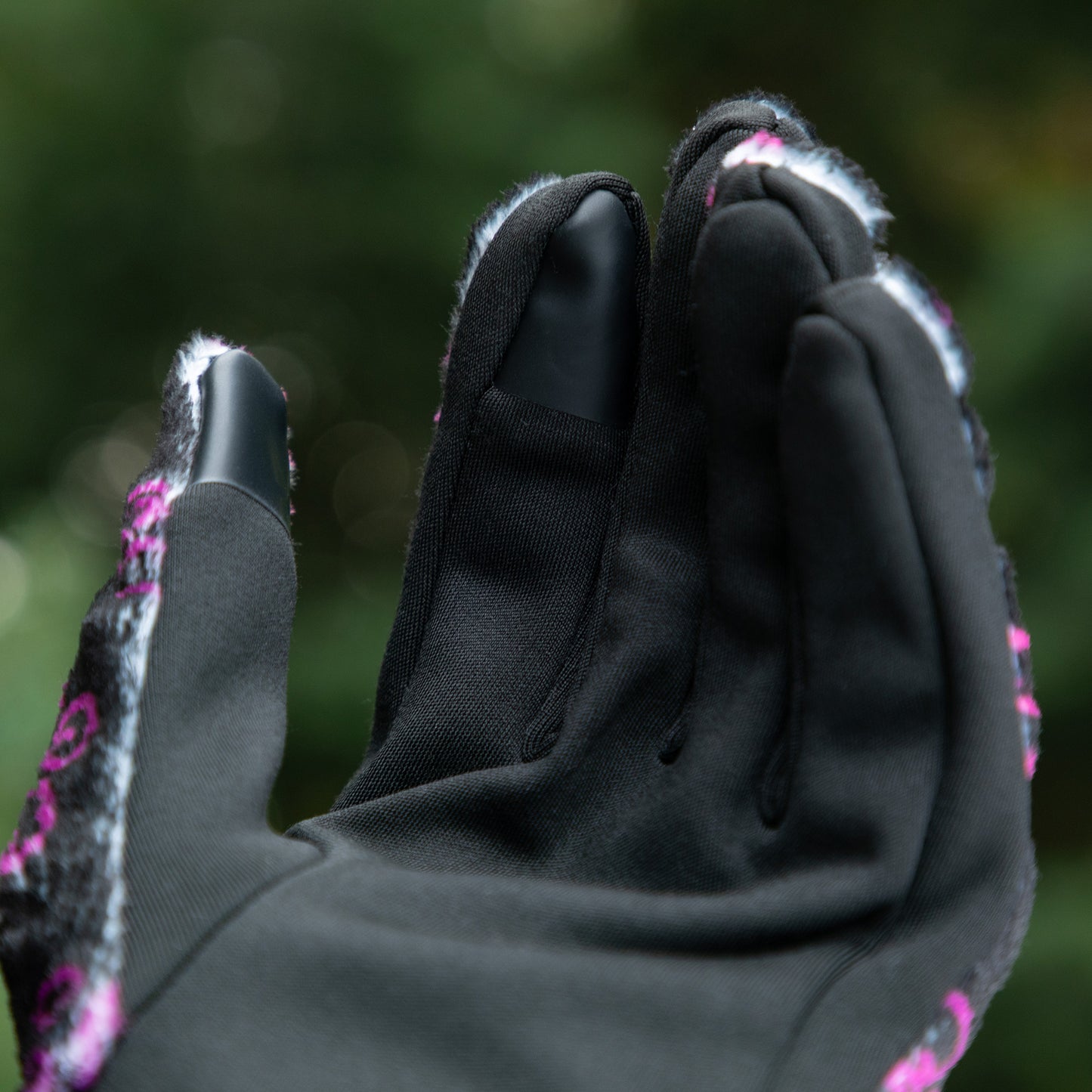 The touchscreen technology fingertips located on the index finger and thumb on a warm black fleece glove adorned with prink and violet elegant paw prints. 