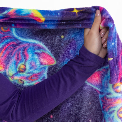 A close-up of a person holding up a plush blanket featuring a colorful cosmic cat design with a purple long-sleeve shirt visible.