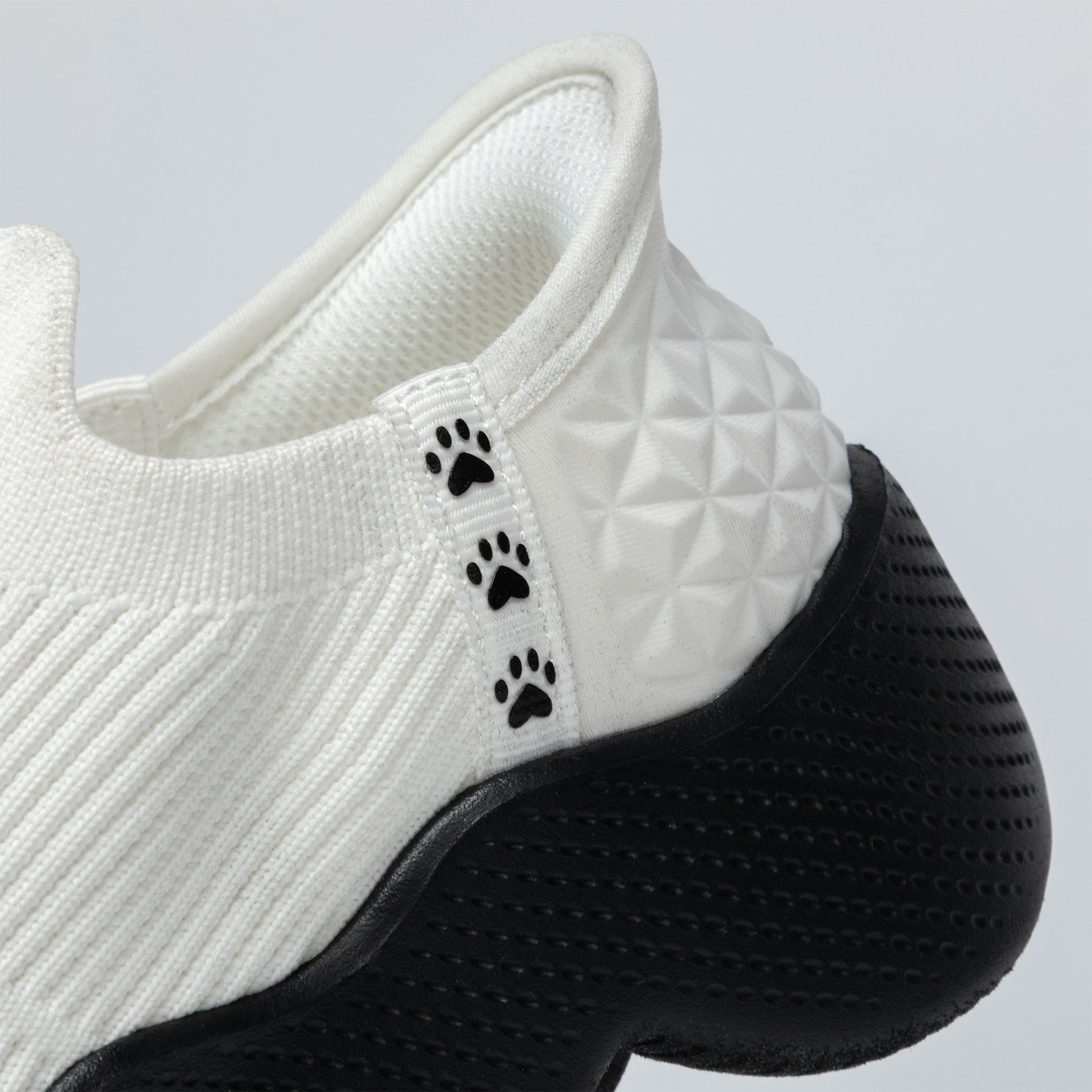White slip-on shoe with black paw prints on a light gray background