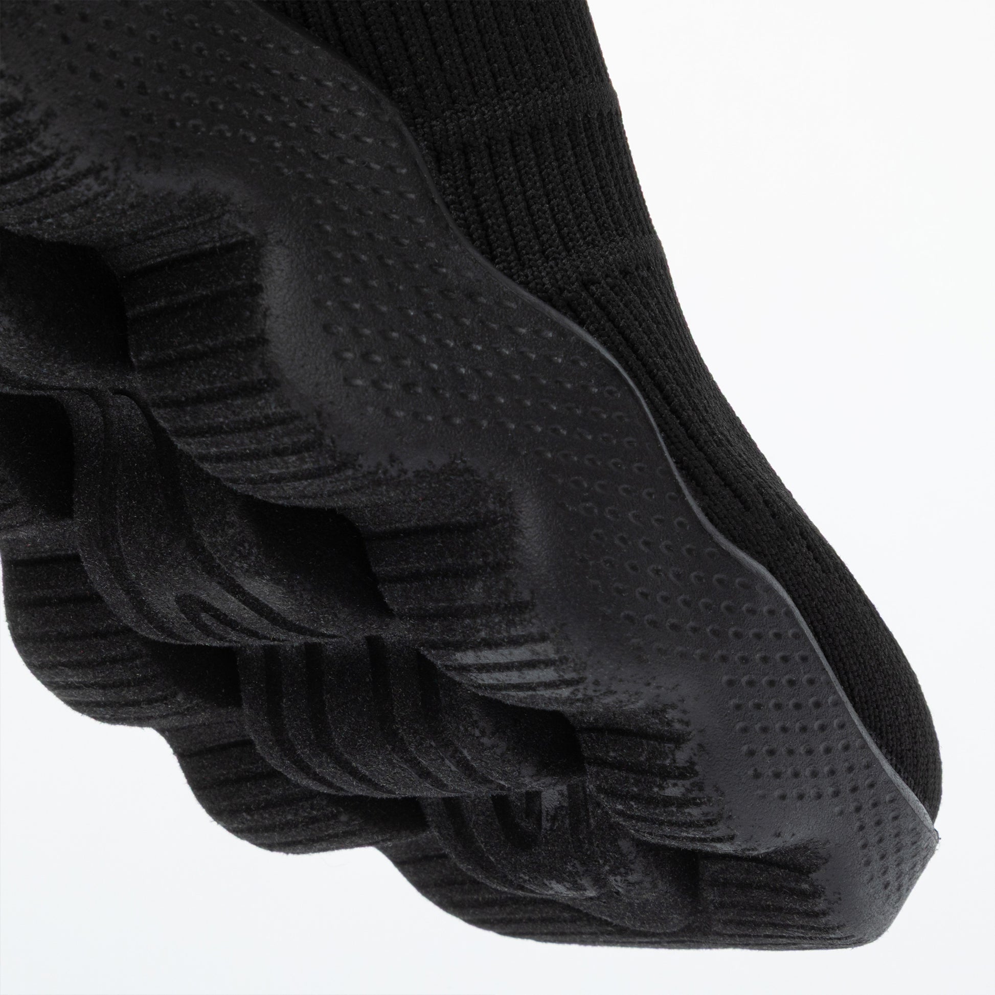 Close up of the deep traction outsole of a black sneaker, on a white background.