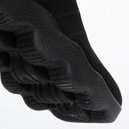Close up of the deep traction outsole of a black sneaker, on a white background.