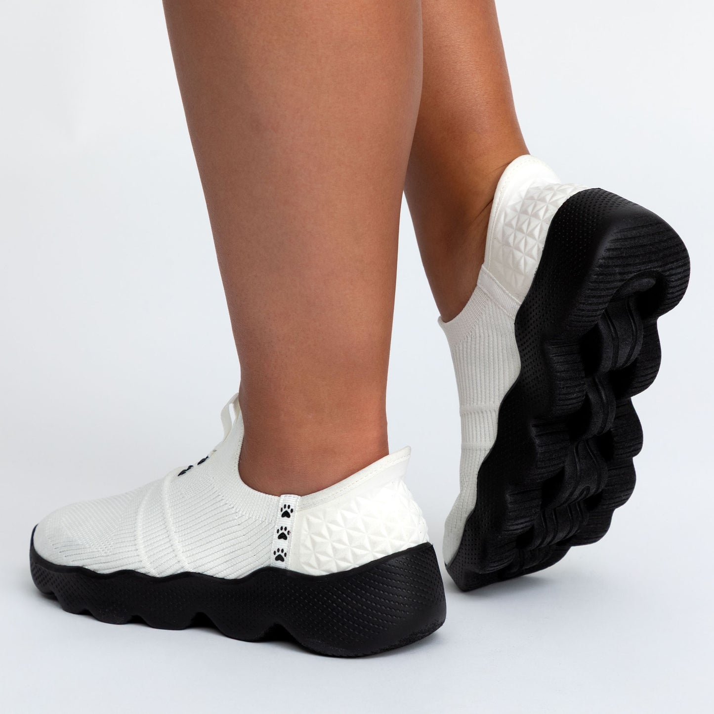 White sneakers with black soles worn by a person on a light gray background