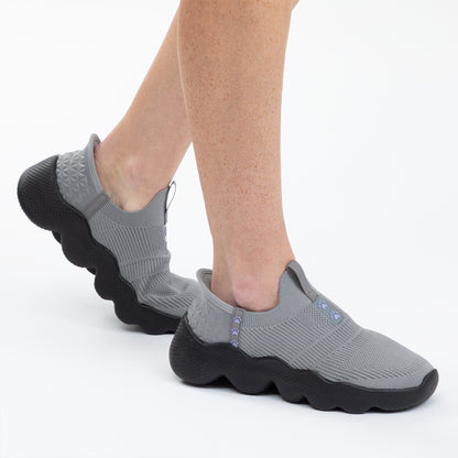 Gray slip-on shoes with black soles worn by a person on a white background