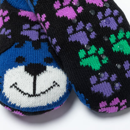 A close-up of a pair of black knit socks featuring a blue and white dog face on one sock and purple paw prints with green paw prints on the other, accented with small sequins.