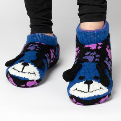 Person wearing blue and rainbow paw patterned knitted slipper socks with a smiling dog face on top, light gray background rainbow dog