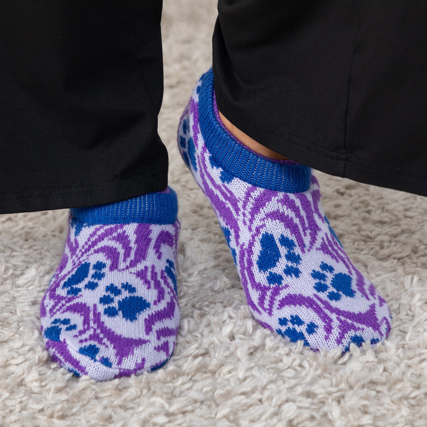 Purple and blue paw patterned knitted slipper socks worn on a carpeted floor Paw Symphony