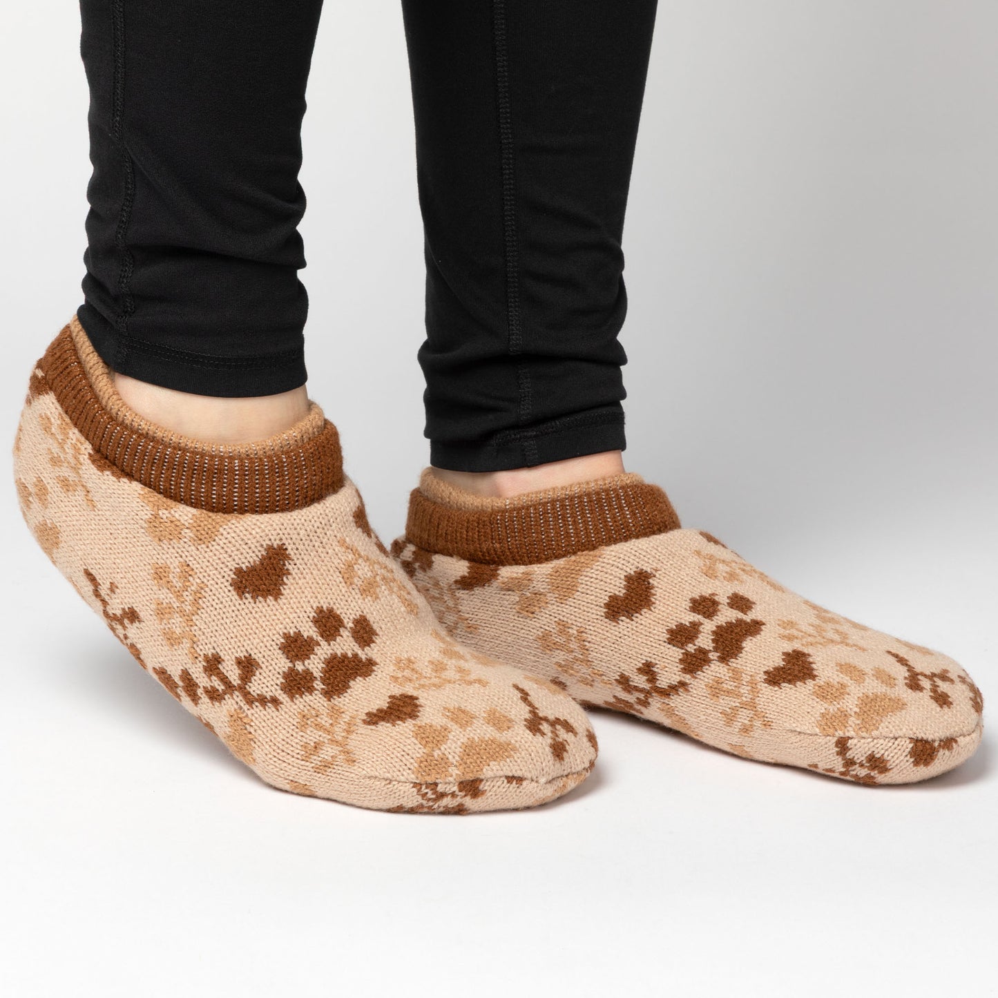 Person wearing brown and beige paw patterned knitted slipper socks, on a white background brown paw sprig