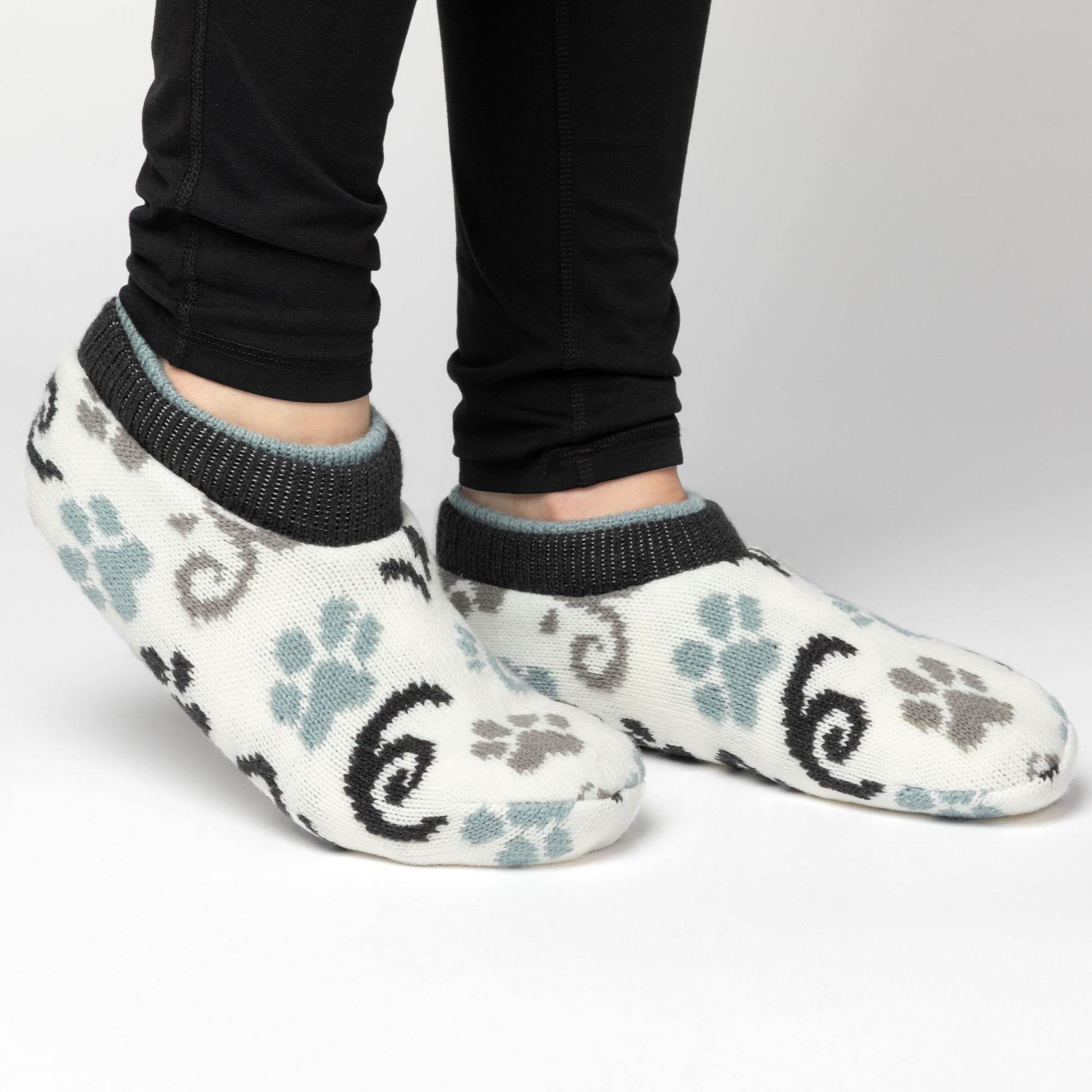 Person wearing white, blue, gray paw patterned knitted slipper socks, on a white background blue gray paws swirls