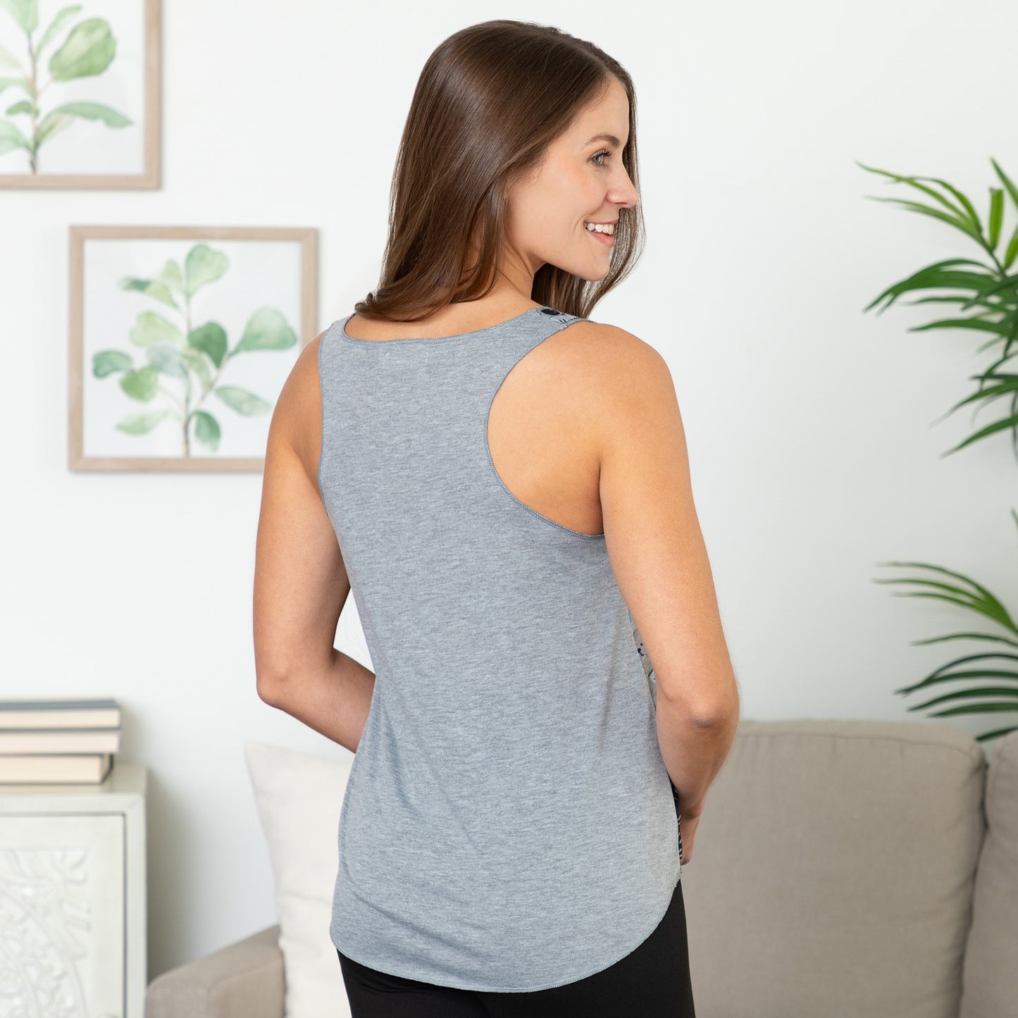 Woman wearing a gray tank top in a living room setting with plants and a couch.