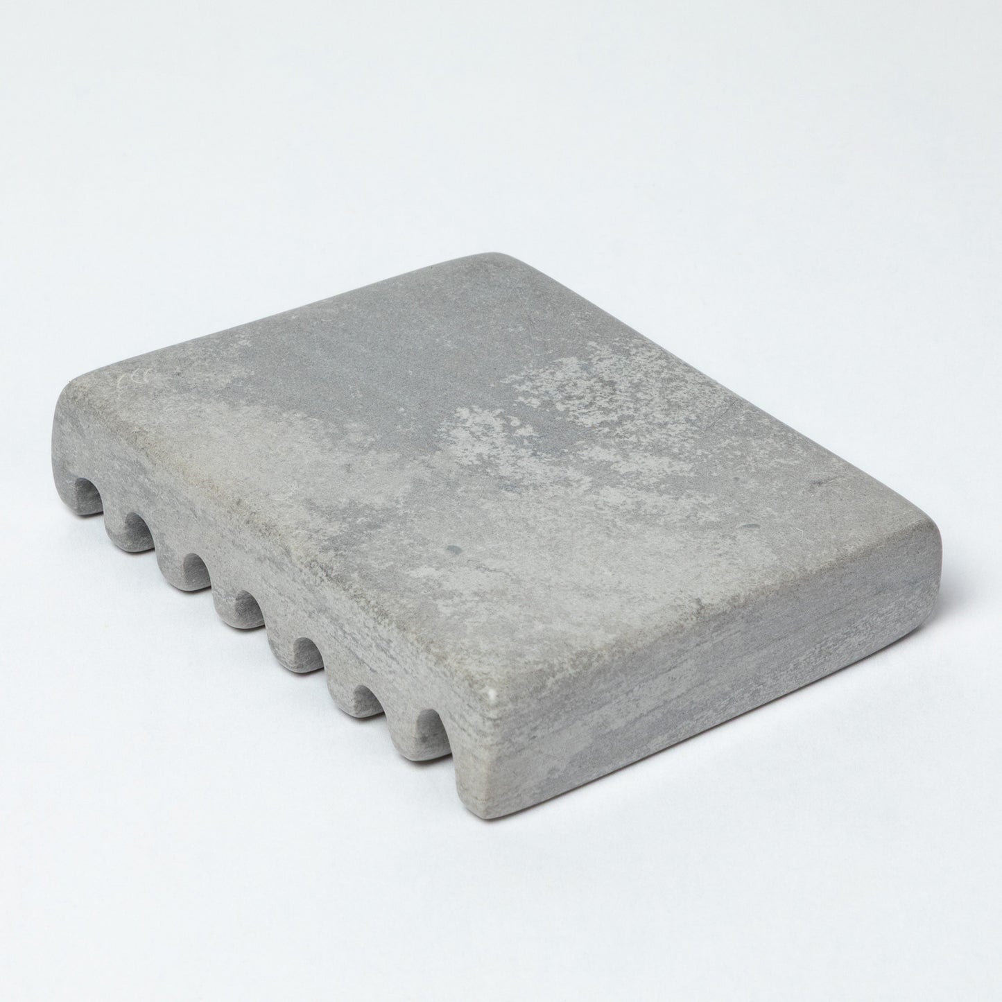 The bottom of a gray soapstone soap dish, against a white background.
