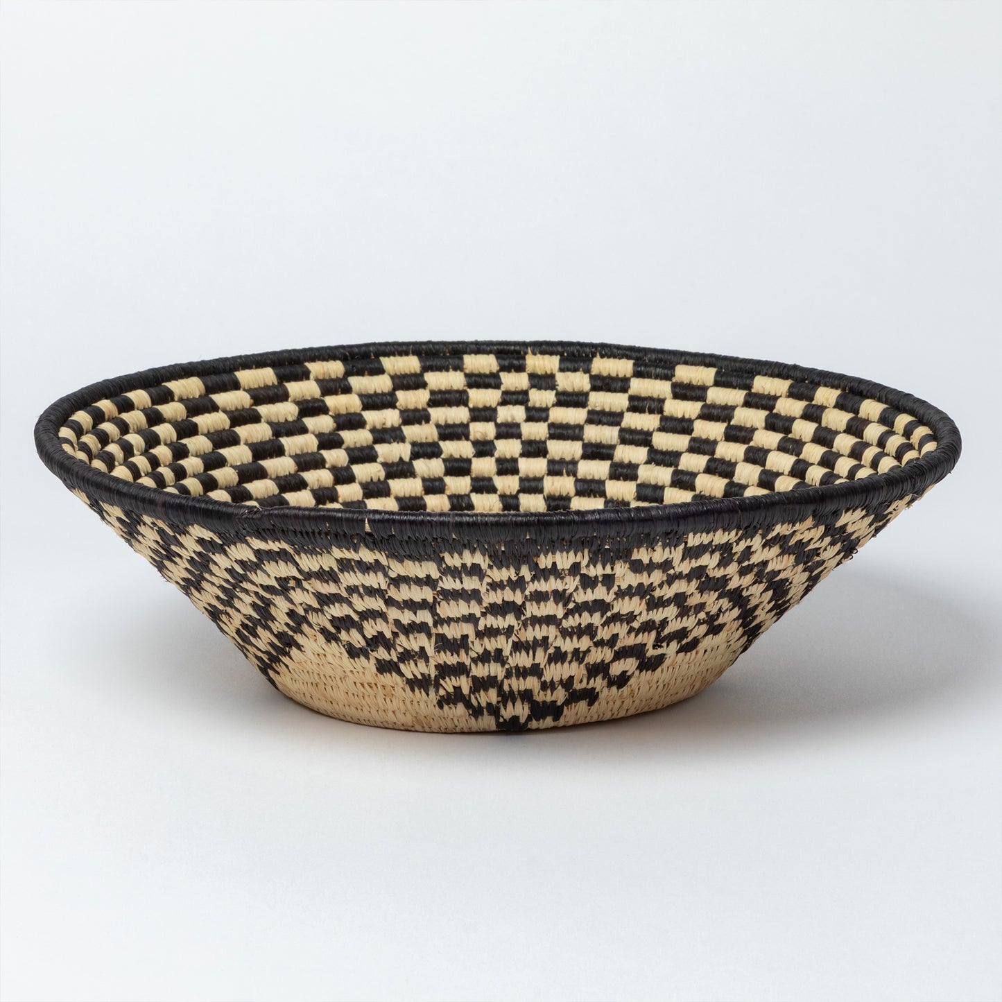 Woven basket with black and natural raffia, with a checkered pattern on a white background