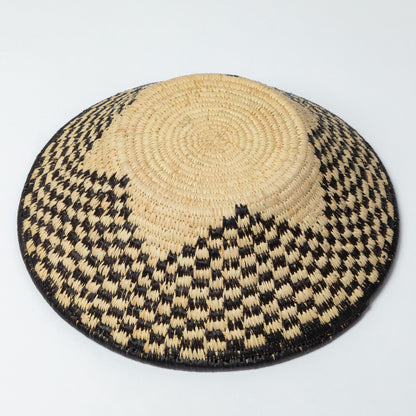 Woven raffia bowl upside down to show bottom and star design on a white background.