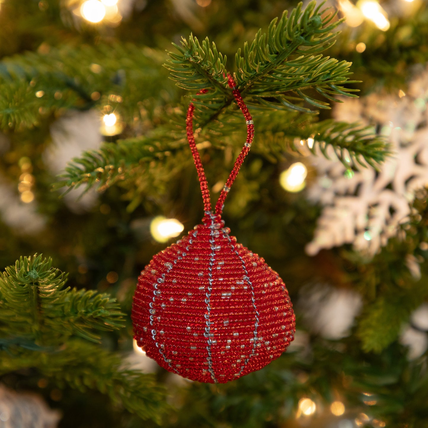 Red beaded ornament hanging on a Christmas tree with blurred lights in the background