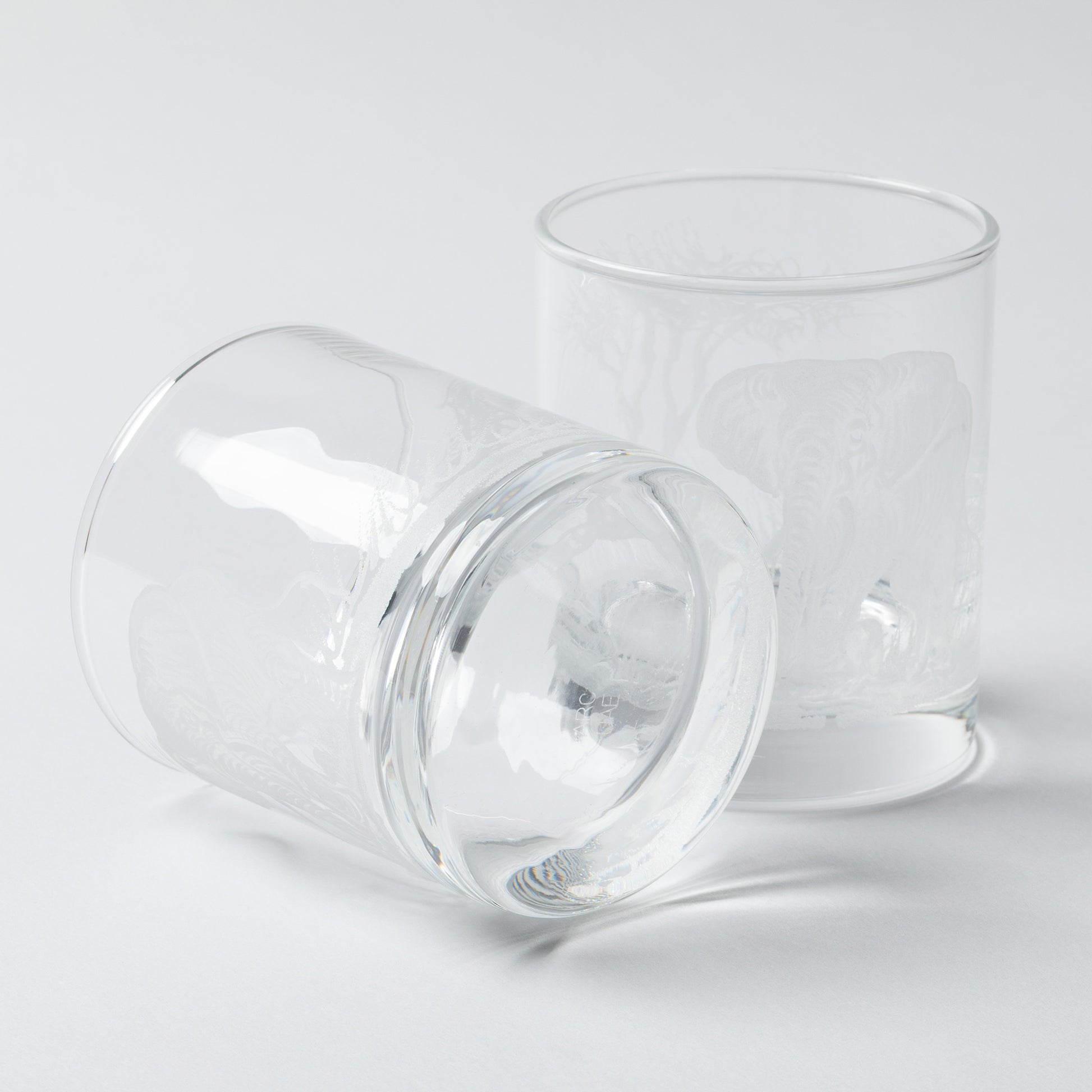 Two clear recycled whiskey glasses on a light gray background