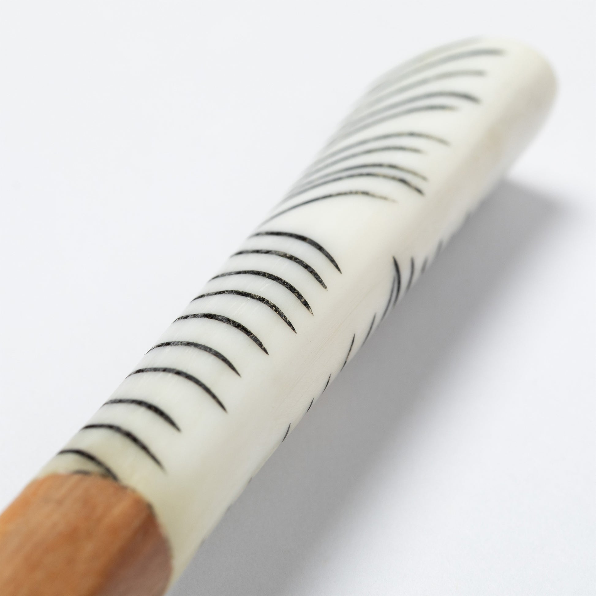 Close-up of a wooden spoon handle with a white bone accent featuring black stripes on a white background.