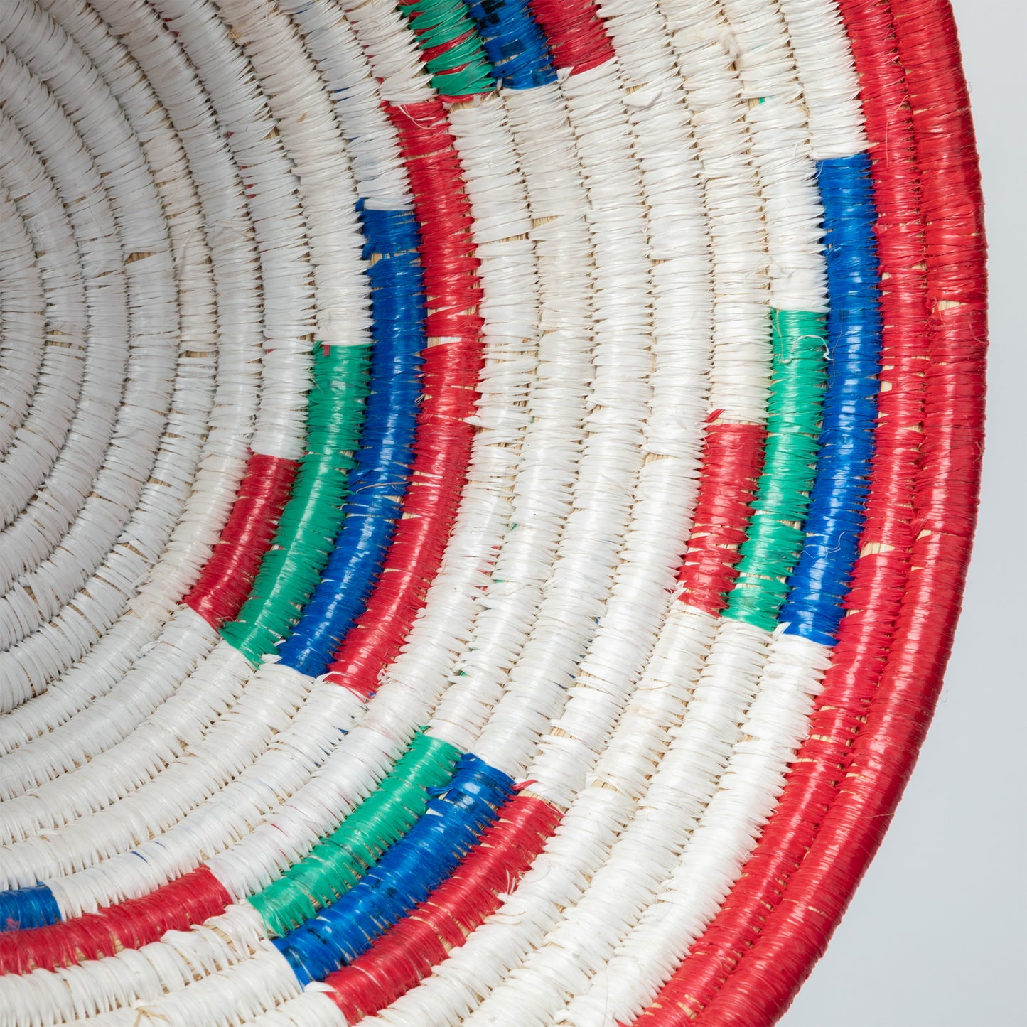 Close-up of a woven basket with red, blue, and green accents on a light gray background