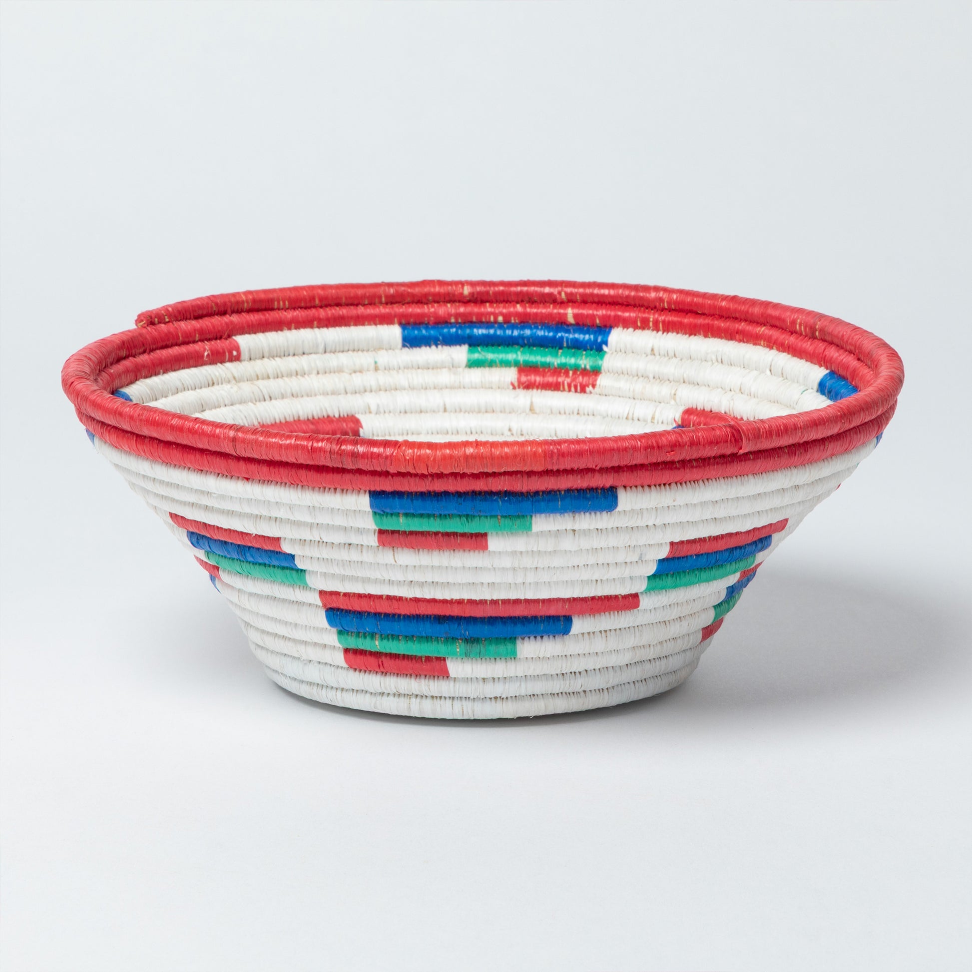 Woven bowl with red, white, blue, and green pattern on a light gray background