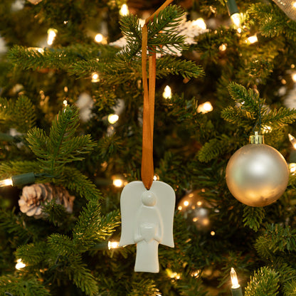 White angel ornament hanging on a Christmas tree with lights and other decorations.