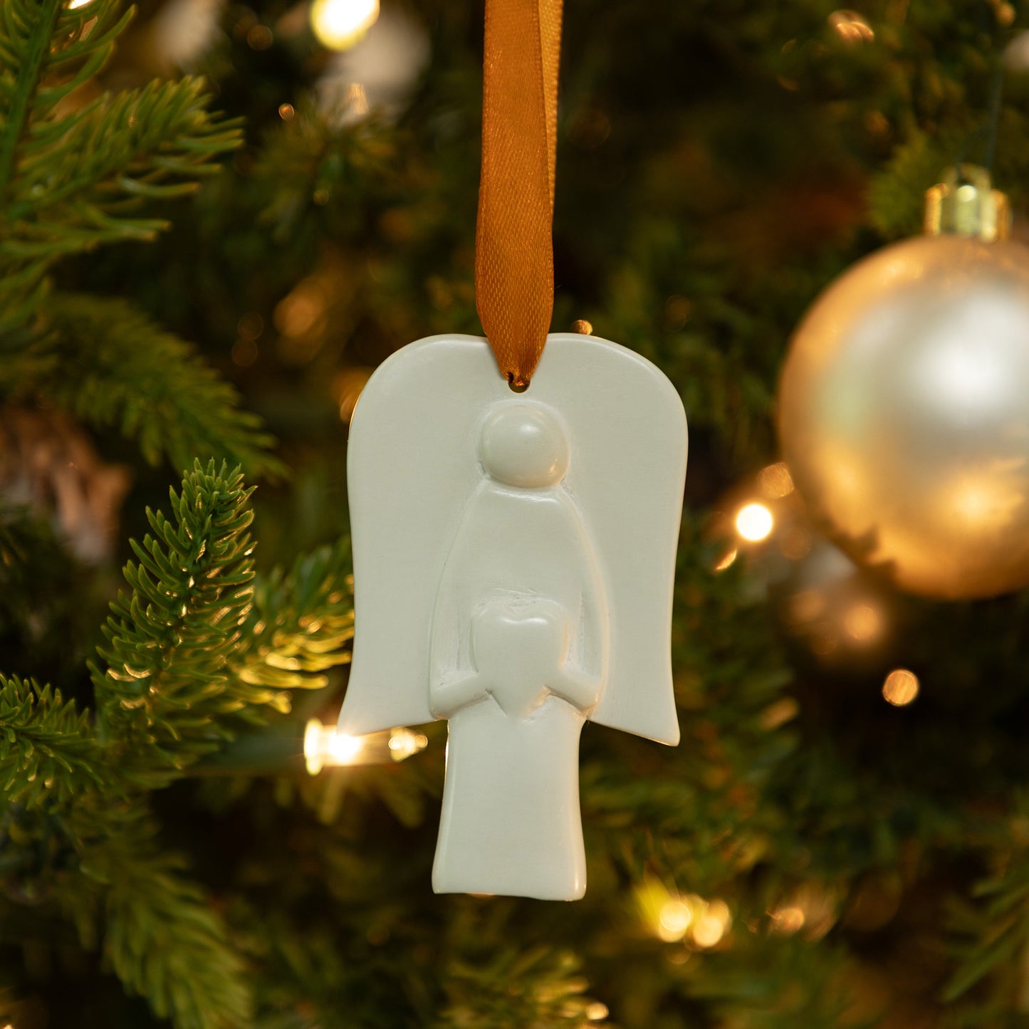 White angel soapstone ornament on a Christmas tree with blurred lights and decorations in the background
