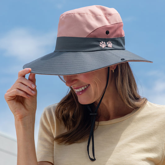 Woman wearing a pink and gray sun hat with a paw print logo against a blue sky.