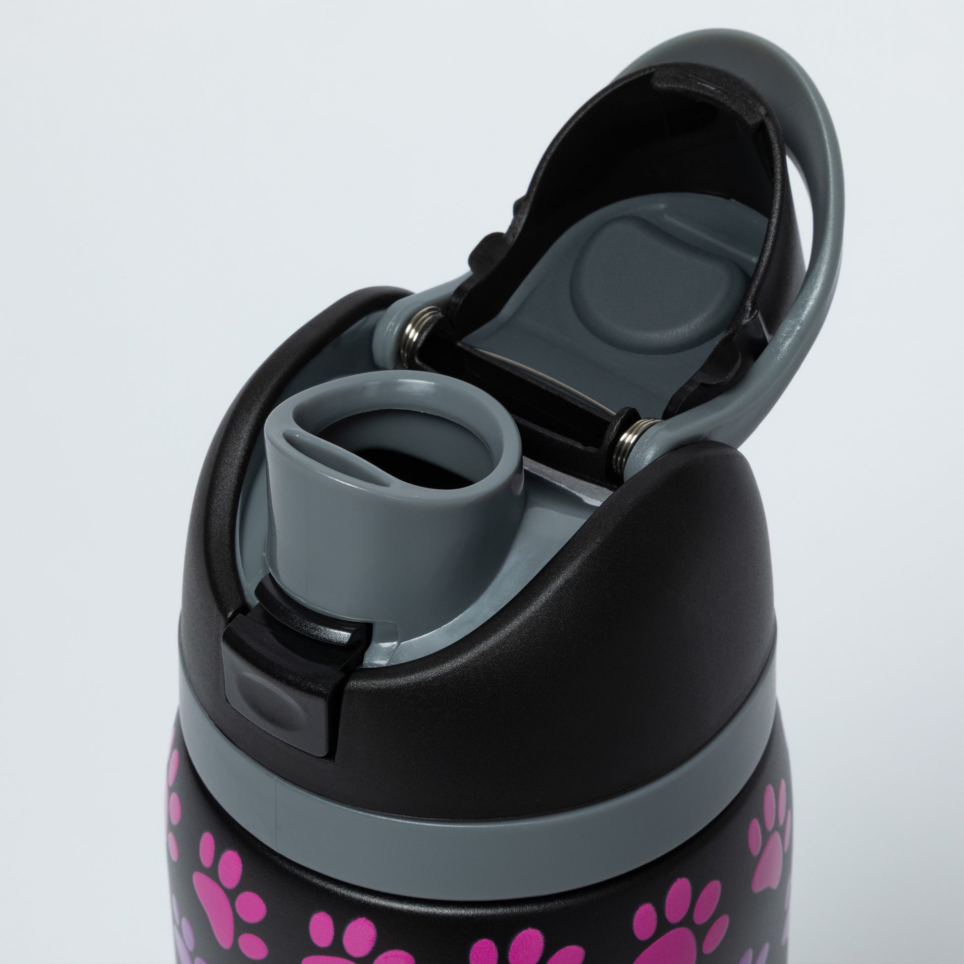 Close-up of a black water bottle with pink paw prints and gray lid on a light gray background