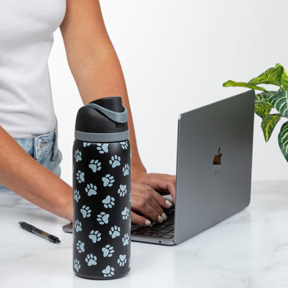 A person types on a laptop beside a paw-print water bottle on a desk.