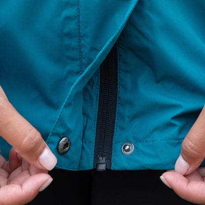 Close-up of a blue rain jacket with a zipper and buttons, held open by hands.
